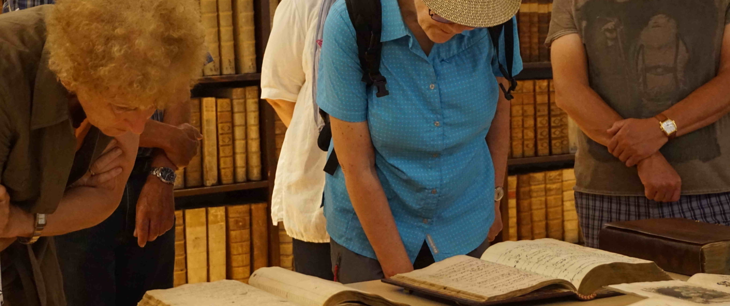 Besucher*innen im Archiv der Uni Salzburg, die einen Blick in die historischen Bücher werfen.